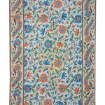 Gulmarg handmade floral rug with chain stitch embroidery in cream and light blue, featuring vibrant orange and blue flowers with green leaves on a soft cotton base.