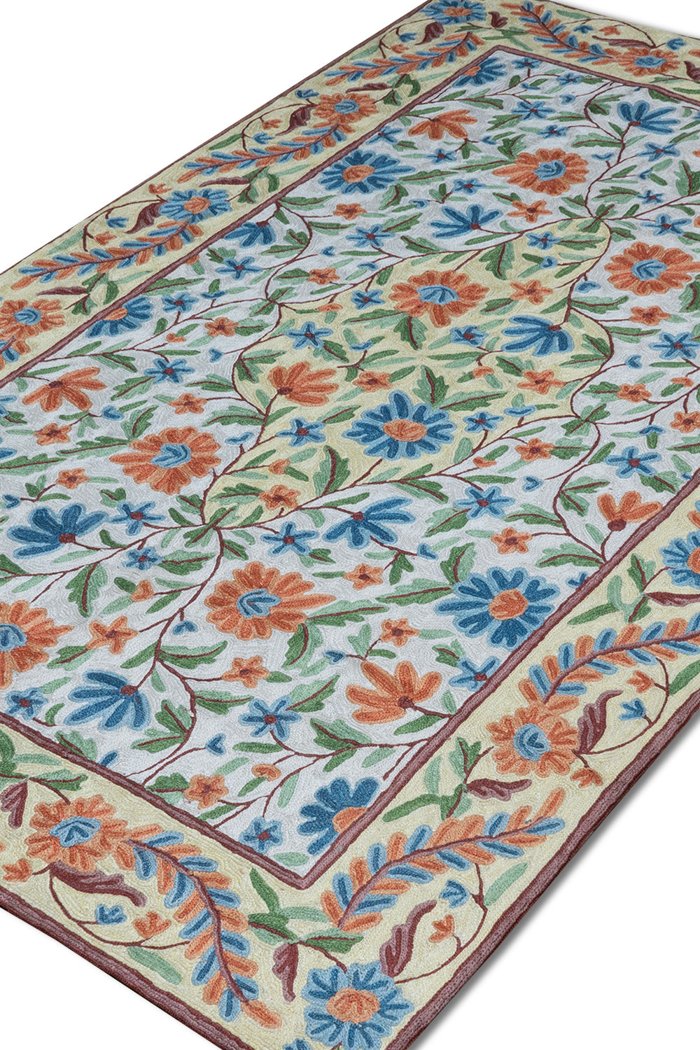 Close-up angled view of the Gulmarg floral rug highlighting intricate chain stitch embroidery and vibrant blue, orange, and green floral patterns on a cream background.