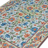 Close-up angled view of the Gulmarg floral rug highlighting intricate chain stitch embroidery and vibrant blue, orange, and green floral patterns on a cream background.