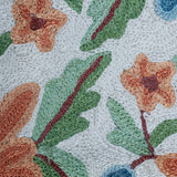 Extreme close-up of the Gulmarg rug showing detailed chain stitch embroidery with textured orange flowers, green leaves, and blue buds on a cream wool background.
