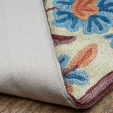 Close-up of the Gulmarg rug corner flipped to reveal the durable cotton backing. The visible floral embroidery on the front showcases textured blue and orange blossoms with maroon outlining on a cream base, resting on a wooden floor.