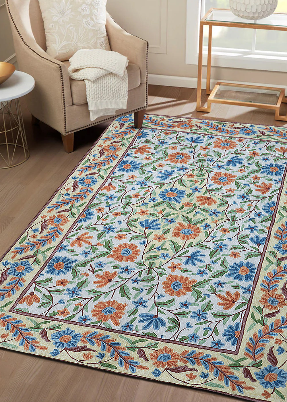Handcrafted Gulmarg floral rug placed in a cozy living room, featuring intricate chain stitch embroidery in cream, blue, orange, and green tones complementing the neutral interior décor.