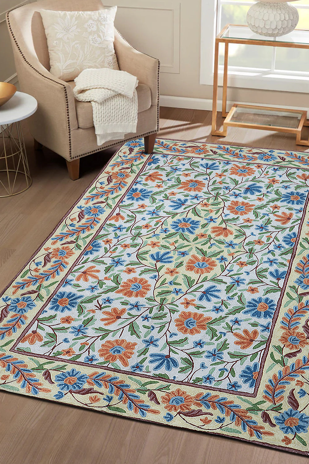 Handcrafted Gulmarg floral rug placed in a cozy living room, featuring intricate chain stitch embroidery in cream, blue, orange, and green tones complementing the neutral interior décor.