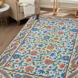 Handcrafted Gulmarg floral rug placed in a cozy living room, featuring intricate chain stitch embroidery in cream, blue, orange, and green tones complementing the neutral interior décor.
