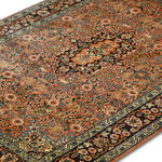  A close-up angled view of the Kirman Peach & Blue Persian Rug, showcasing its intricate floral motifs, delicate arabesques, and a striking central medallion. The detailed craftsmanship and warm peach tones contrast beautifully with the deep blue border, highlighting the timeless elegance of Persian rug-making.