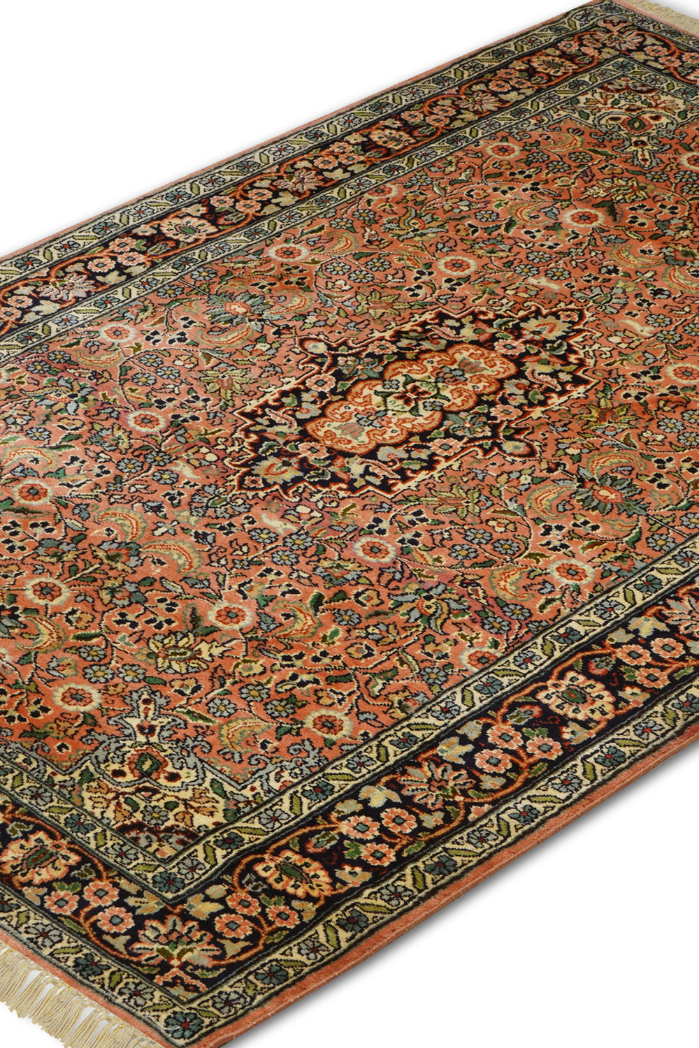  A close-up angled view of the Kirman Peach & Blue Persian Rug, showcasing its intricate floral motifs, delicate arabesques, and a striking central medallion. The detailed craftsmanship and warm peach tones contrast beautifully with the deep blue border, highlighting the timeless elegance of Persian rug-making.