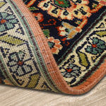 A close-up view of a Kirman Persian rug with a folded corner, showcasing its intricate floral border design and tightly woven backing. The rich navy, peach, and green hues highlight the traditional craftsmanship, while the rug's thickness and fine weave structure are clearly visible. The rug is placed on a light wooden floor, adding contrast to its ornate patterns.