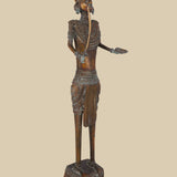 Antique-style dark brass statue of a soldier holding a sword pointing upwards and with an open palm extended, wearing textured armor and a distinctive headdress, standing on a tiered base.