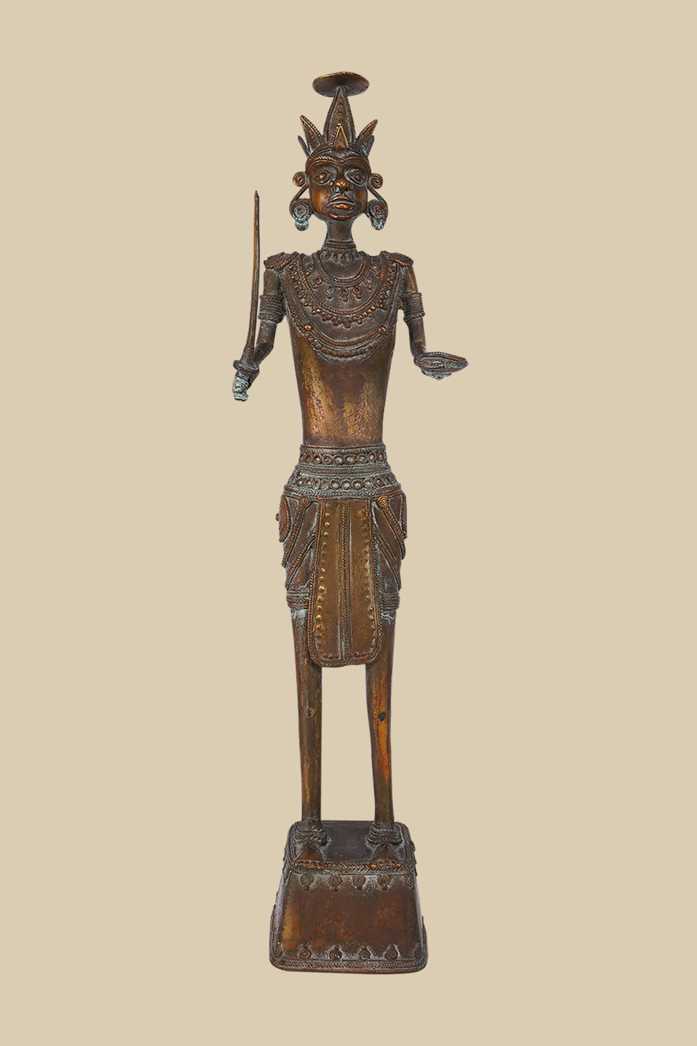 Antique dark brass sculpture of an Indian soldier, possibly tribal, holding a sword and with an open hand, adorned with traditional jewelry and a distinctive headdress, standing on a decorated base.