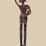 ack view of an antique dark brass sculpture of a village woman carrying a child in her arm and a pot on her head, showing the details of her posture, the child, and the pot's placement. The sculpture stands on a decorated base.