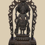 Four-armed dark brass idol of Lord Vishnu standing on a lotus pedestal within a decorative arch. He holds the conch (shankha), discus (chakra), a lotus (padma), and a mace (gada), symbolizing his divine power and preservation.