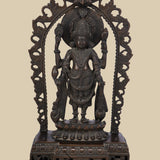 Four-armed dark brass idol of Lord Vishnu standing on a lotus pedestal within a decorative arch. He holds the conch (shankha), discus (chakra), a lotus (padma), and a mace (gada), symbolizing his divine power and preservation.