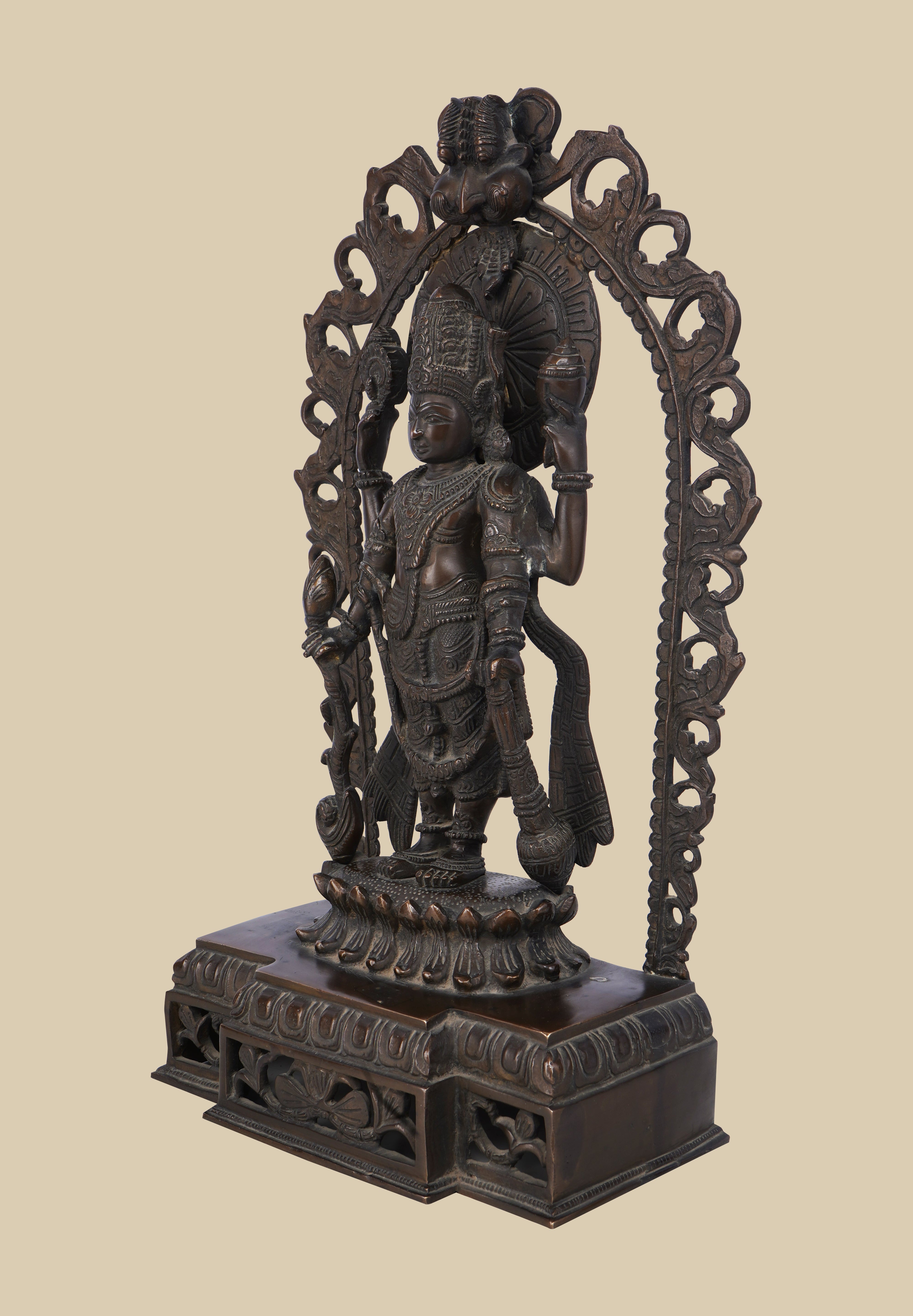 Dark brass sculpture of the Hindu god Lord Vishnu, depicted with four arms holding his sacred symbols within an elaborately carved arch and standing on a detailed pedestal.