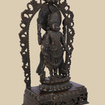 Ornate dark brass statue of Lord Vishnu standing beneath a decorative arch, holding his four symbolic attributes: the conch, discus, lotus, and mace. The intricate carving and traditional design are prominent.