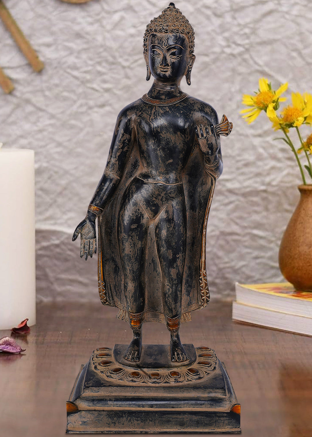 Standing brass figure of Lord Buddha with one hand extended in a gesture of blessing or teaching, wearing simple robes with ornate borders and standing on a decorative lotus pedestal.