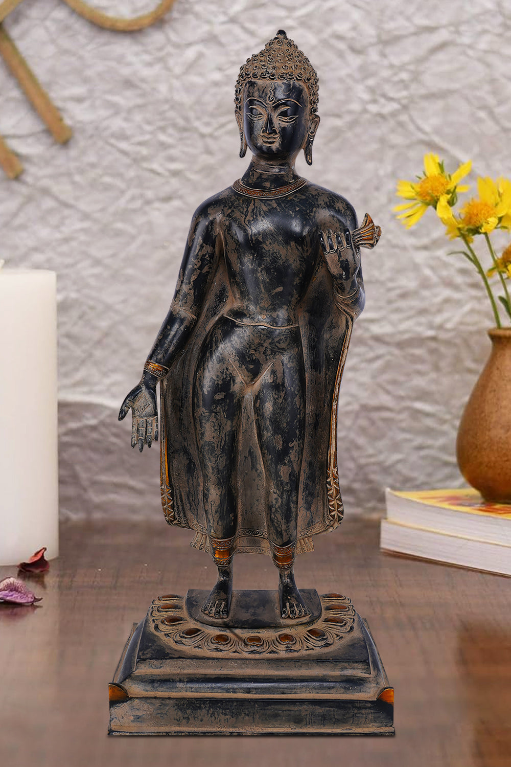 Standing brass figure of Lord Buddha with one hand extended in a gesture of blessing or teaching, wearing simple robes with ornate borders and standing on a decorative lotus pedestal.