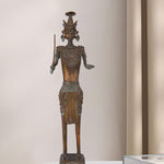 Dark brass figure of a tribal warrior holding a sword in one hand and an open palm in the other, featuring intricate jewelry, a unique headdress, and standing on a decorated pedestal.