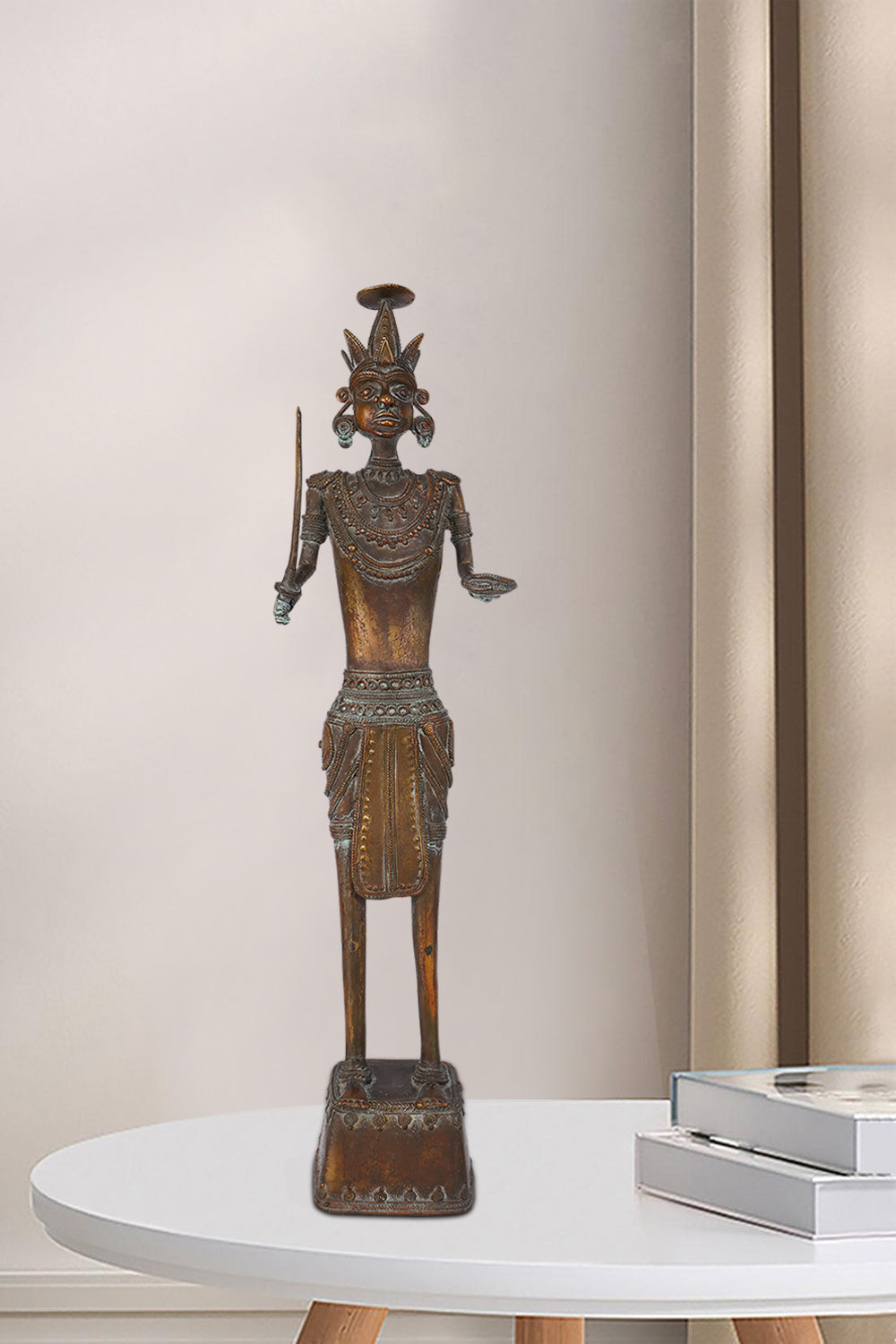 Dark brass figure of a tribal warrior holding a sword in one hand and an open palm in the other, featuring intricate jewelry, a unique headdress, and standing on a decorated pedestal.