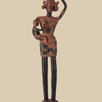 Antique dark brass sculpture of a tribal woman carrying a child in her arms and a pot on her head, adorned with traditional jewelry and standing on a decorated pedestal. The artwork reflects rural life and motherhood.